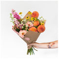 Golden Hour Bouquet featuring orange dahlias, ranunculus, pink gerbera daisies, yellow rudbeckia, chamomile, stock flowers and hypericum berries in kraft paper wrap
